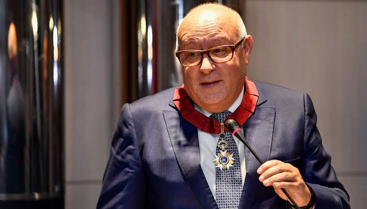Saïd Alj speaking at a podium, wearing a state decoration on a red ribbon